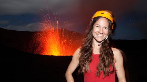 Die Fotografin Ulla Lohmann mit Helm auf dem Vulkan Yasur in Vanuatu mit Feuer im Hintergrund
