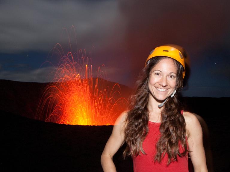 Die Fotografin Ulla Lohmann mit Helm auf dem Vulkan Yasur in Vanuatu mit Feuer im Hintergrund