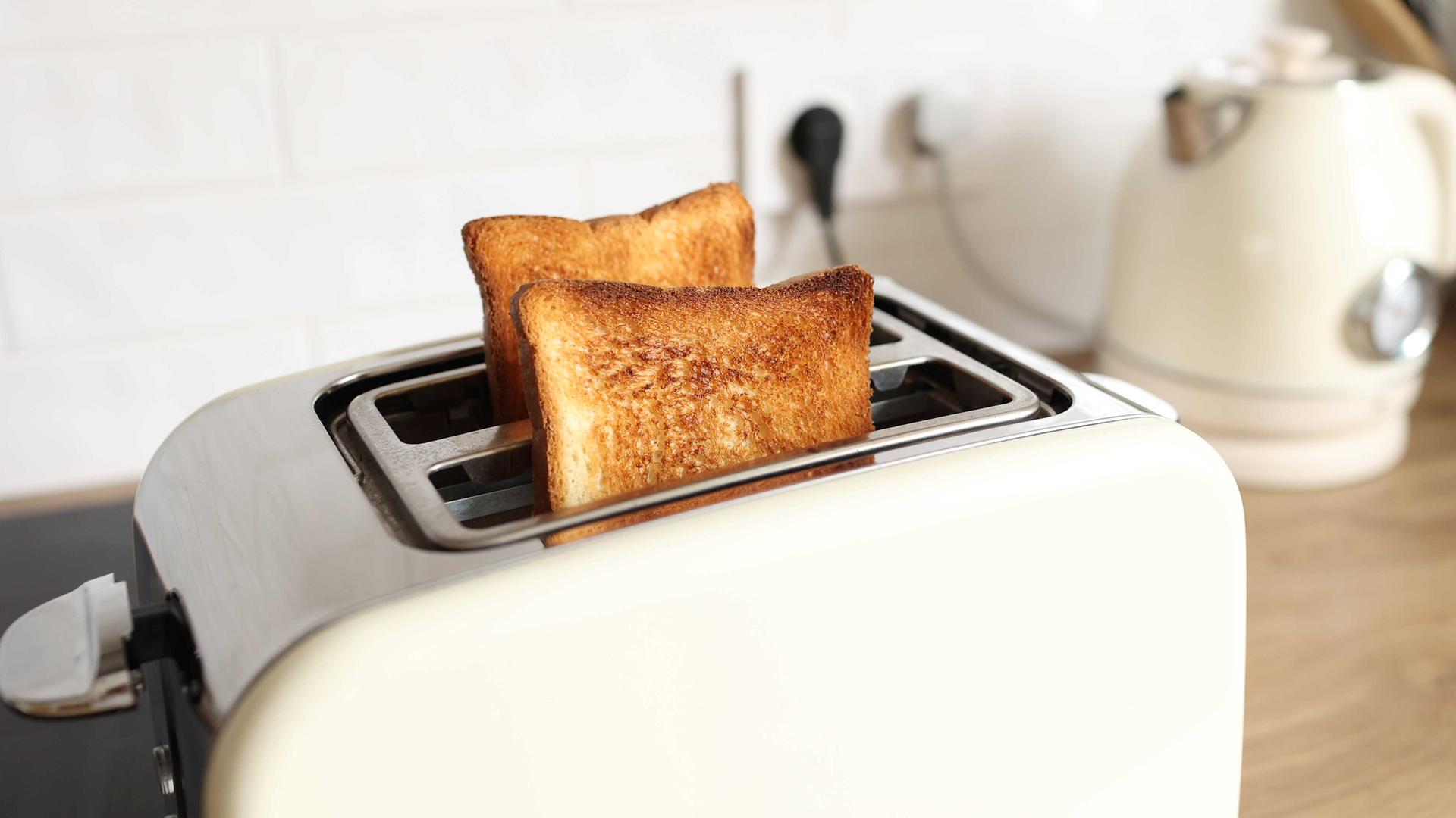 Ein weißer Toaster mit zwei gebackenen Scheiben Toast. Ein weißer Toaster mit zwei gebackenen Scheiben Toast.