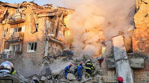 Feuerwehrleute arbeiten an der Stelle eines brennenden Gebäudes nach einem russischen Angriff in Kiew, Ukraine.
      