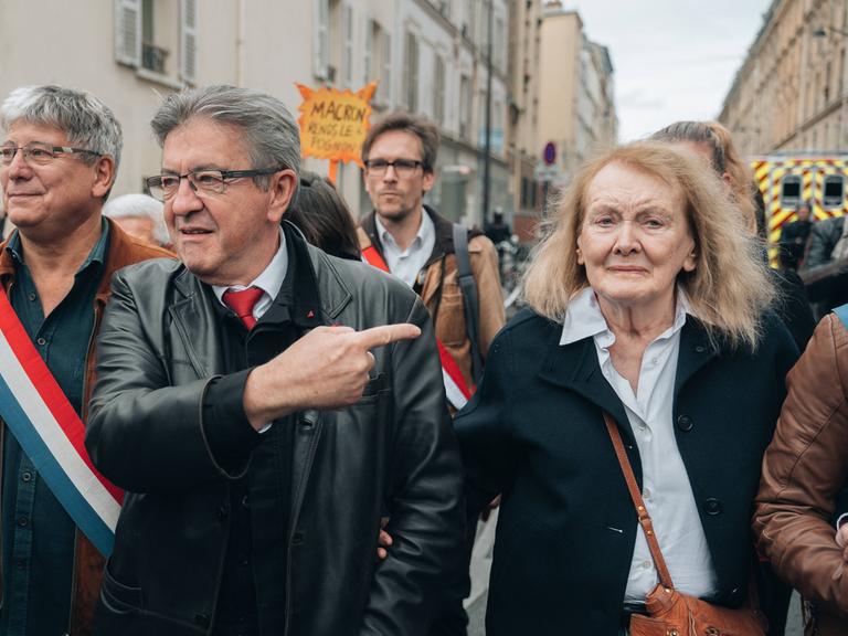 Literaturnobelpreisträgerin Annie Ernaux demonstriert in Paris mit vielen anderen Menschen. Links von ihr der Linkspopulist Jean-Luc Mélenchon, der auf sie zeigt.