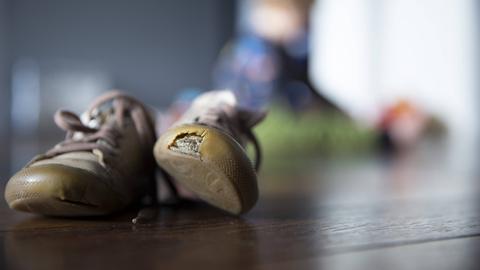Ein paar Kinderschuhe, wobei der linke Schuh eine großes Loch hat.