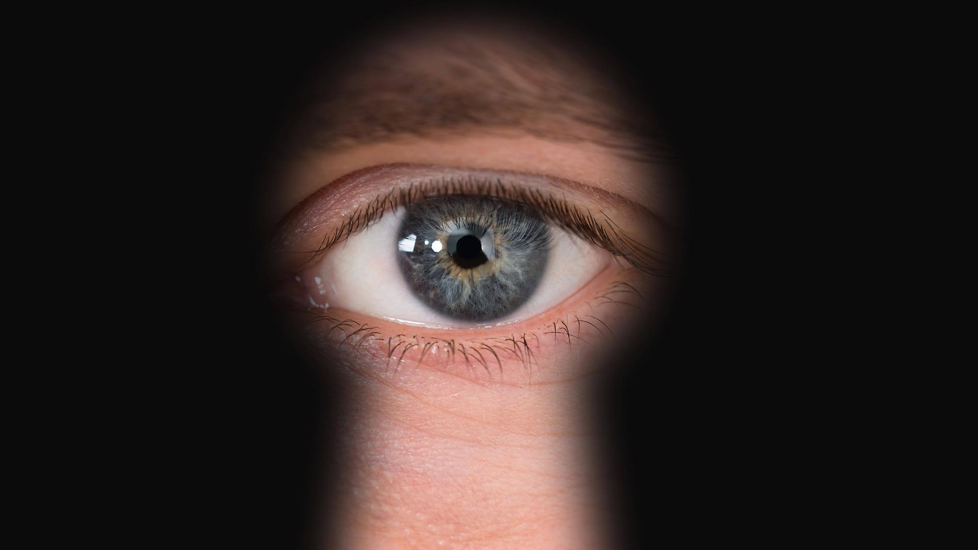 Ein blau-graues Auge ist durch ein Schlüsselloch zu sehen.