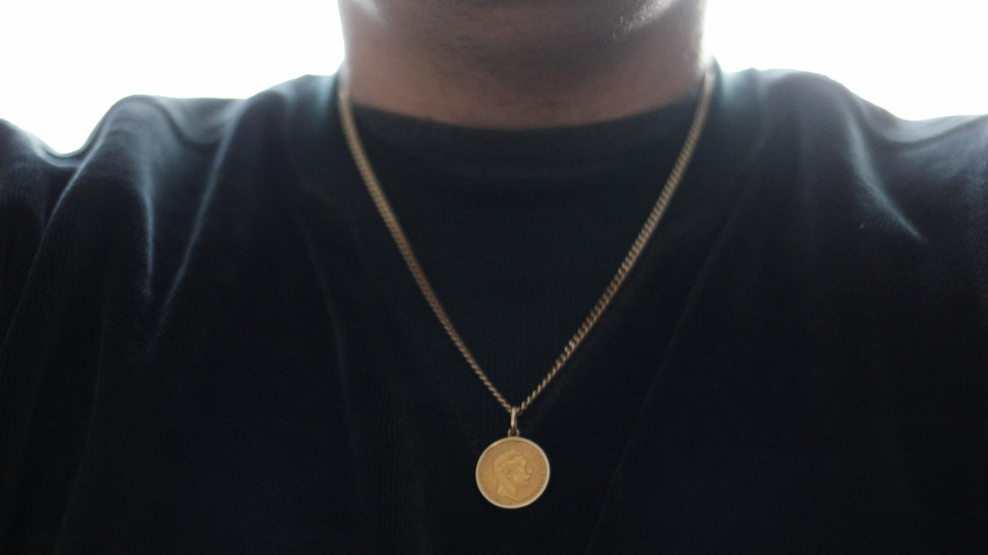 Eine goldene Münze hängt an einer goldenen Kette um den Hals. 