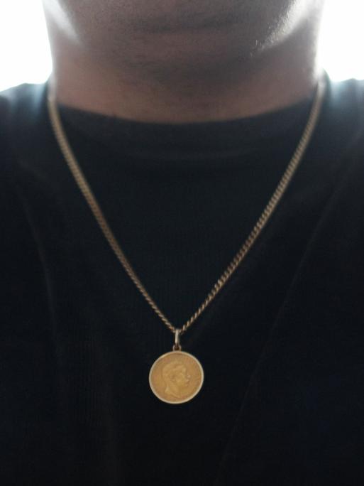 Eine goldene Münze hängt an einer goldenen Kette um den Hals. 