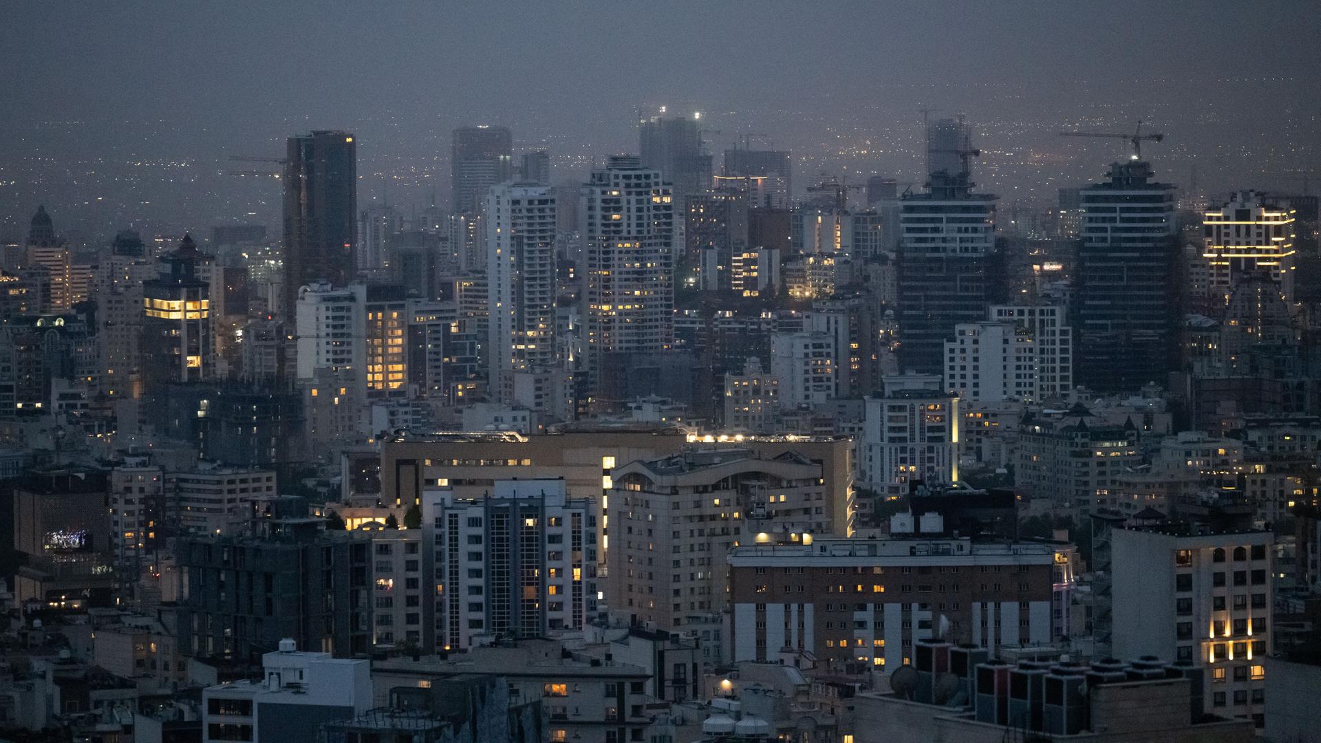 Die Skyline der Millionenmetropole Teheran in der Abenddämmerung. Einige Fenster der Hochhäuser leuchten noch nach Sonnenuntergang.