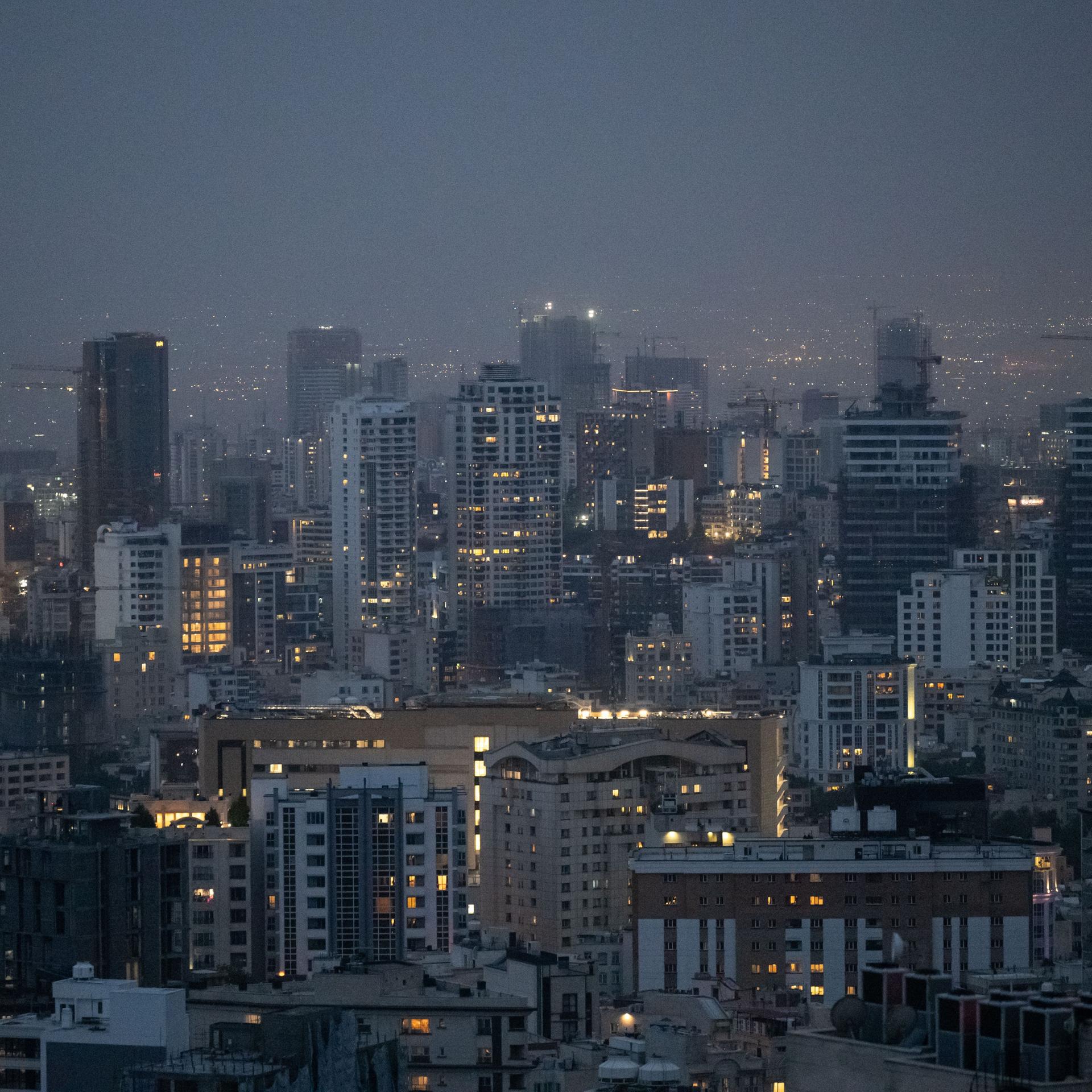 Die Skyline der Millionenmetropole Teheran in der Abenddämmerung. Einige Fenster der Hochhäuser leuchten noch nach Sonnenuntergang.