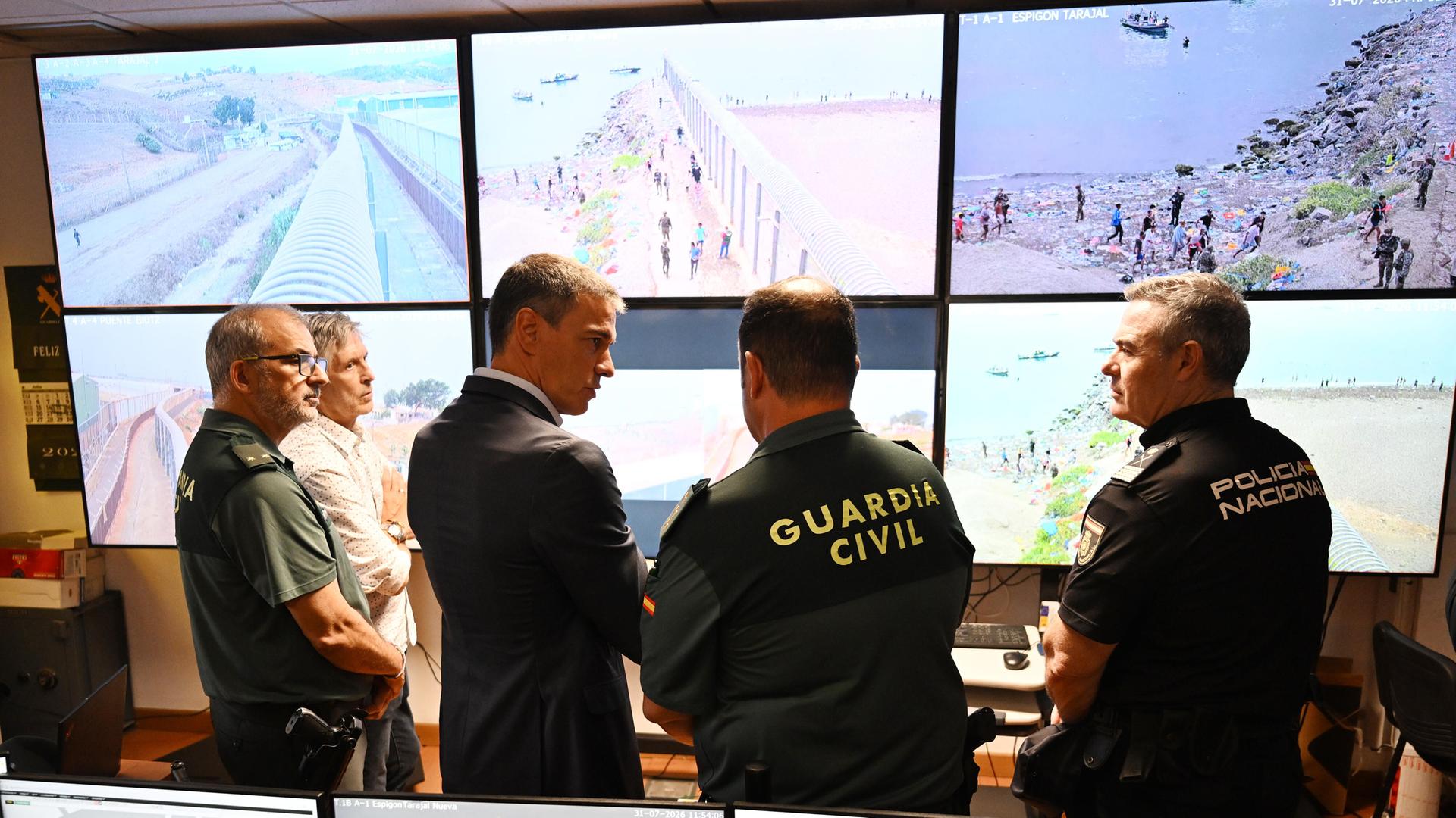 Der spanische Ministerpräsident Sanchez bei seinem Besuch in Ceuta - Er spricht mit Mitarbeitern der Guardia Civil in einem Lagezentrum; im Hintergrund sind Bildschirme zu sehen, die die Lage vor Ort zeigen.
      