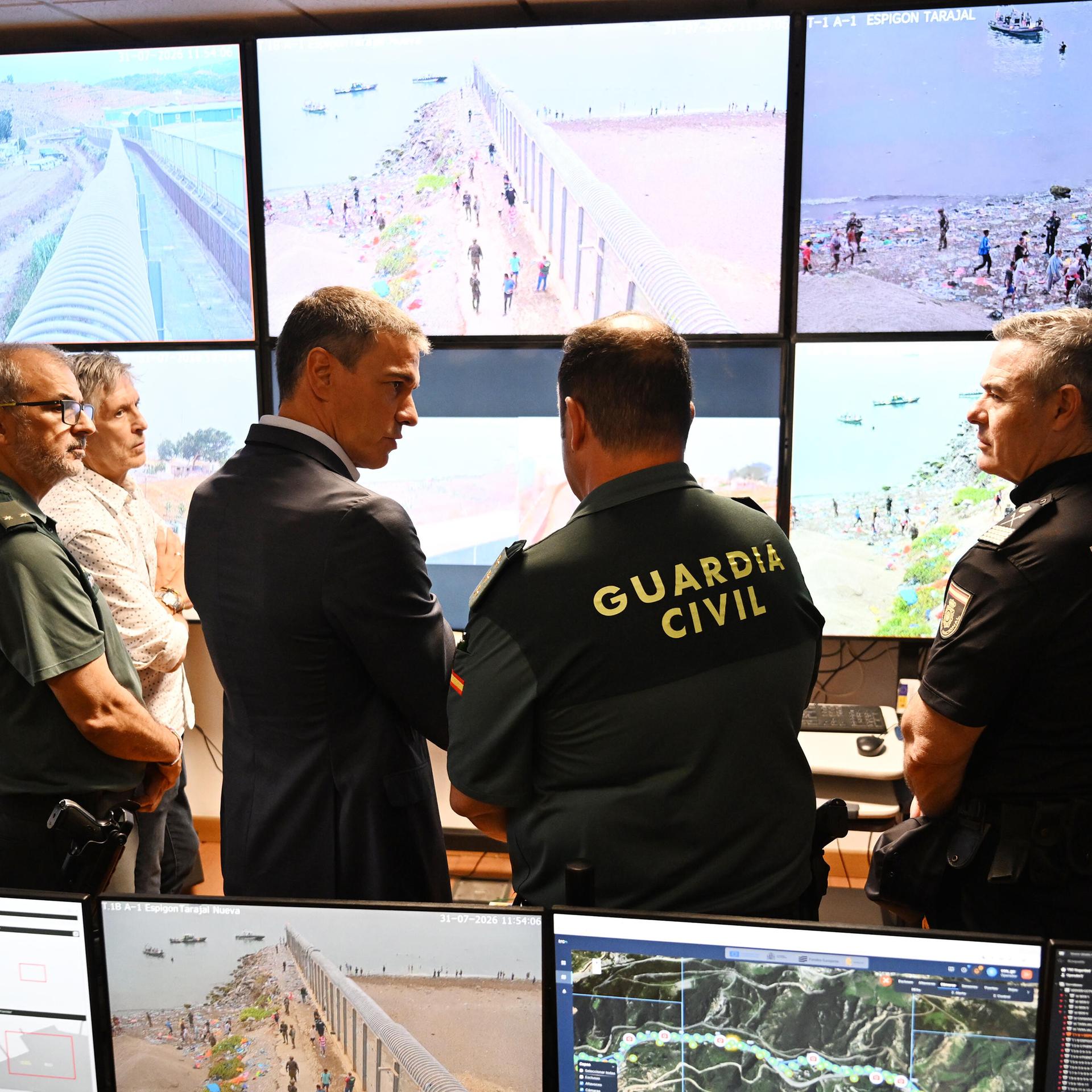 Der spanische Ministerpräsident Sanchez bei seinem Besuch in Ceuta - Er spricht mit Mitarbeitern der Guardia Civil in einem Lagezentrum; im Hintergrund sind Bildschirme zu sehen, die die Lage vor Ort zeigen. 
