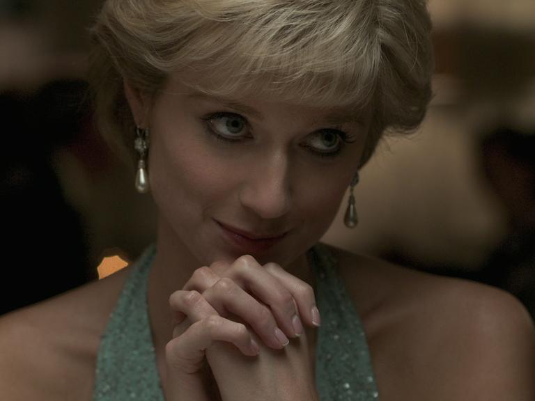 Die Schauspielerin Elizabeth Debicki spielt in der Erfolgsserie "The Crown" Prizessin Diana. Sie hat die Hände unter dem Kinn gefaltet und blickt verträumt nach rechts.