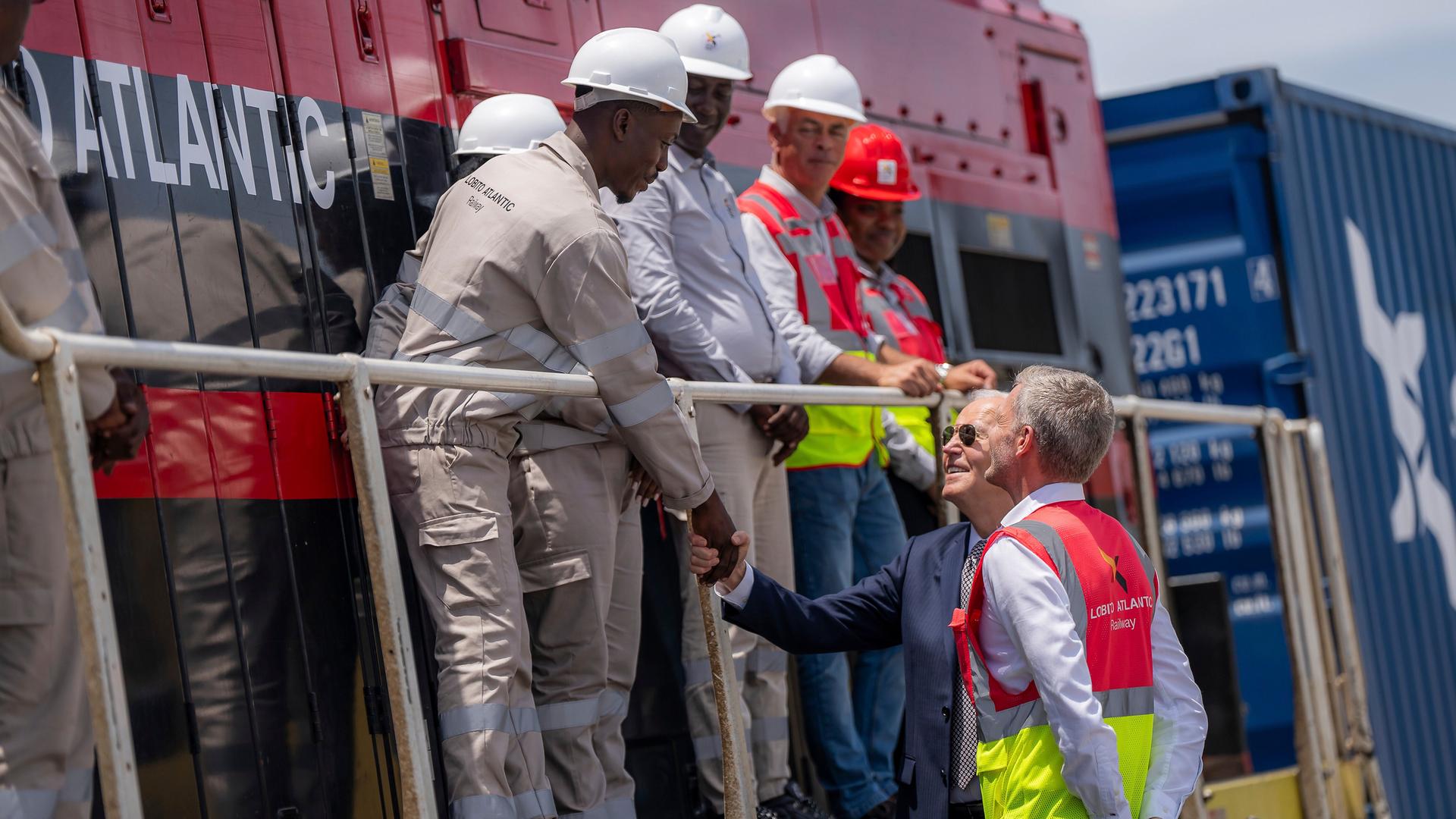 Der ehemalige US-Präsident Joe Biden (Mitte) begrüßt zusammen mit dem Betriebsleiter Nicolas Gregoir (rechts) Arbeiter während einer Besichtigung der Lobito Atlantic Railway im Hafen von Lobito am 4. Dezember 2024 in Angola.