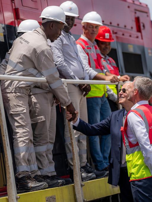 Der ehemalige US-Präsident Joe Biden (Mitte) begrüßt zusammen mit dem Betriebsleiter Nicolas Gregoir (rechts) Arbeiter während einer Besichtigung der Lobito Atlantic Railway im Hafen von Lobito am 4. Dezember 2024 in Angola.