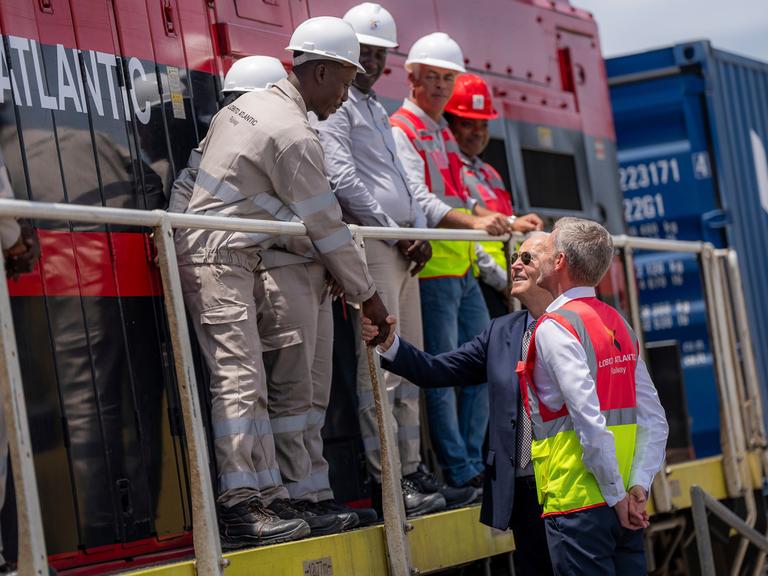 Der ehemalige US-Präsident Joe Biden (Mitte) begrüßt zusammen mit dem Betriebsleiter Nicolas Gregoir (rechts) Arbeiter während einer Besichtigung der Lobito Atlantic Railway im Hafen von Lobito am 4. Dezember 2024 in Angola.