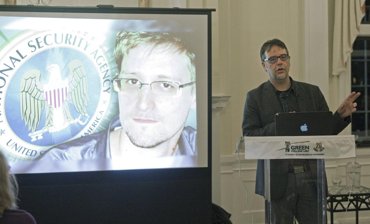 Ein Herr steht an einem Pult und referiert neben einem Bildschirm, auf dem ein Porträt des US-amerikanischen Whistleblowers Edward Snowden zu sehen ist.