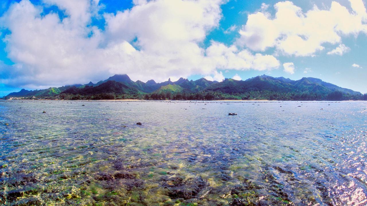 Blick auf die Gebirgskette einer Insel am Horizont, im Vordergrund das flache Meer mit Vulkangestein