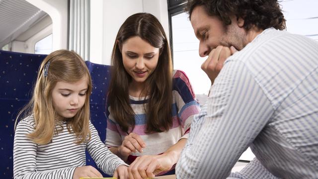 Eine Familie spielt Karten an einem Tisch in einem Abteil von der Deutschen Bahn.