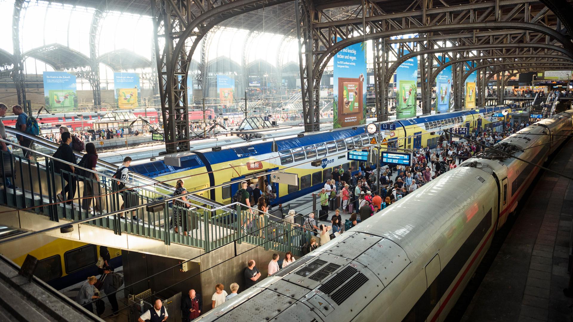 Blick in den Hamburger Hauptbahnhof mit Fahrgästen auf Bahnsteigen und Zügen unter einem Stahldach