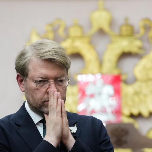 Das Bild zeigt Rybakow vor Gericht. Er hält seine Hände flach aneinandergelegt vor dem Mund. Im Hintergrund ist das russische Staatswappen zu erkennen.