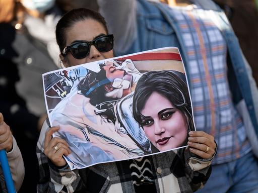 Eine Iranerin beteiligt sich vor dem US-Konsulat in Frankfurt an einer Demonstration gegen das Regime im Iran. Dabei hält sie ein Plakat mit dem Bild der 22-jährigen Mahsa Amini in den Händen.
