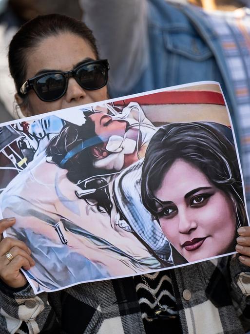 Eine Iranerin beteiligt sich vor dem US-Konsulat in Frankfurt an einer Demonstration gegen das Regime im Iran. Dabei hält sie ein Plakat mit dem Bild der 22-jährigen Mahsa Amini in den Händen.