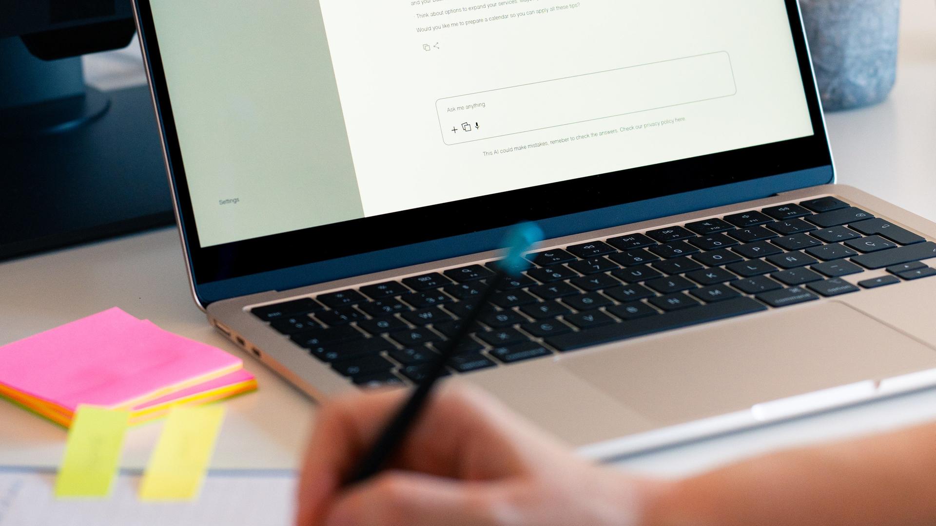 Eine Person hat einen KI-Chatbot auf einem Laptop geöffnet und macht daneben handschriftliche Notizen auf einem Block. Eine Person hat einen KI-Chatbot auf einem Laptop geöffnet und macht daneben handschriftliche Notizen auf einem Block.