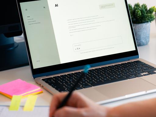 Eine Person hat einen KI-Chatbot auf einem Laptop geöffnet und macht daneben handschriftliche Notizen auf einem Block. Eine Person hat einen KI-Chatbot auf einem Laptop geöffnet und macht daneben handschriftliche Notizen auf einem Block.