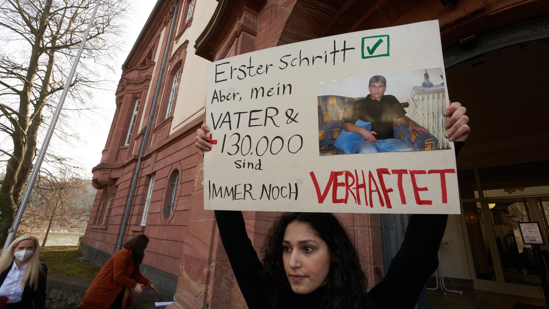 Eine Demonstrantin hält vor einem Gerichtsgebäude ein Plakat hoch. Auf diesem steht "Erster Schritt, aber mein Vater und 130.000 andere sind immer noch in Haft".