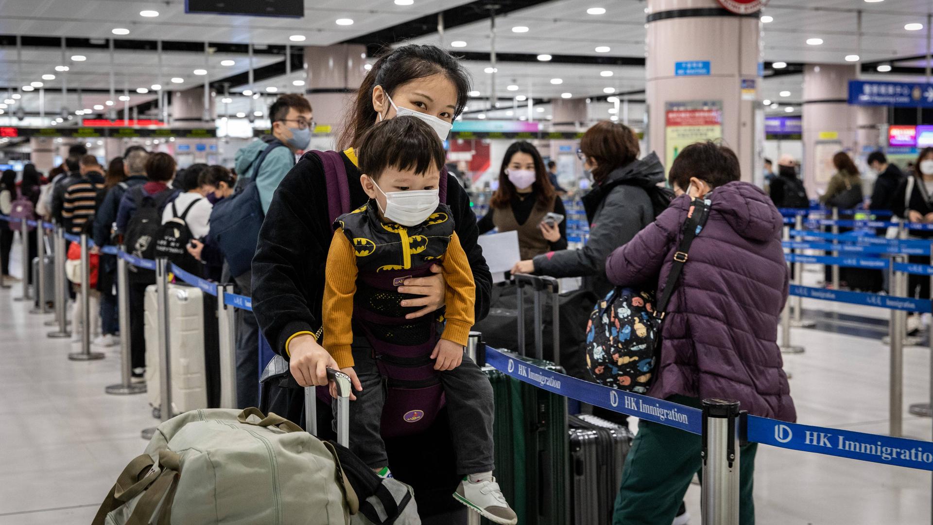 Eine Chinesin trägt ihr Kind an den Körper gebunden in einem Flughafen.
