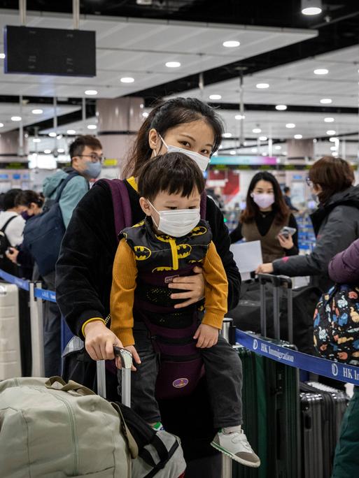 Eine Chinesin trägt ihr Kind an den Körper gebunden in einem Flughafen.