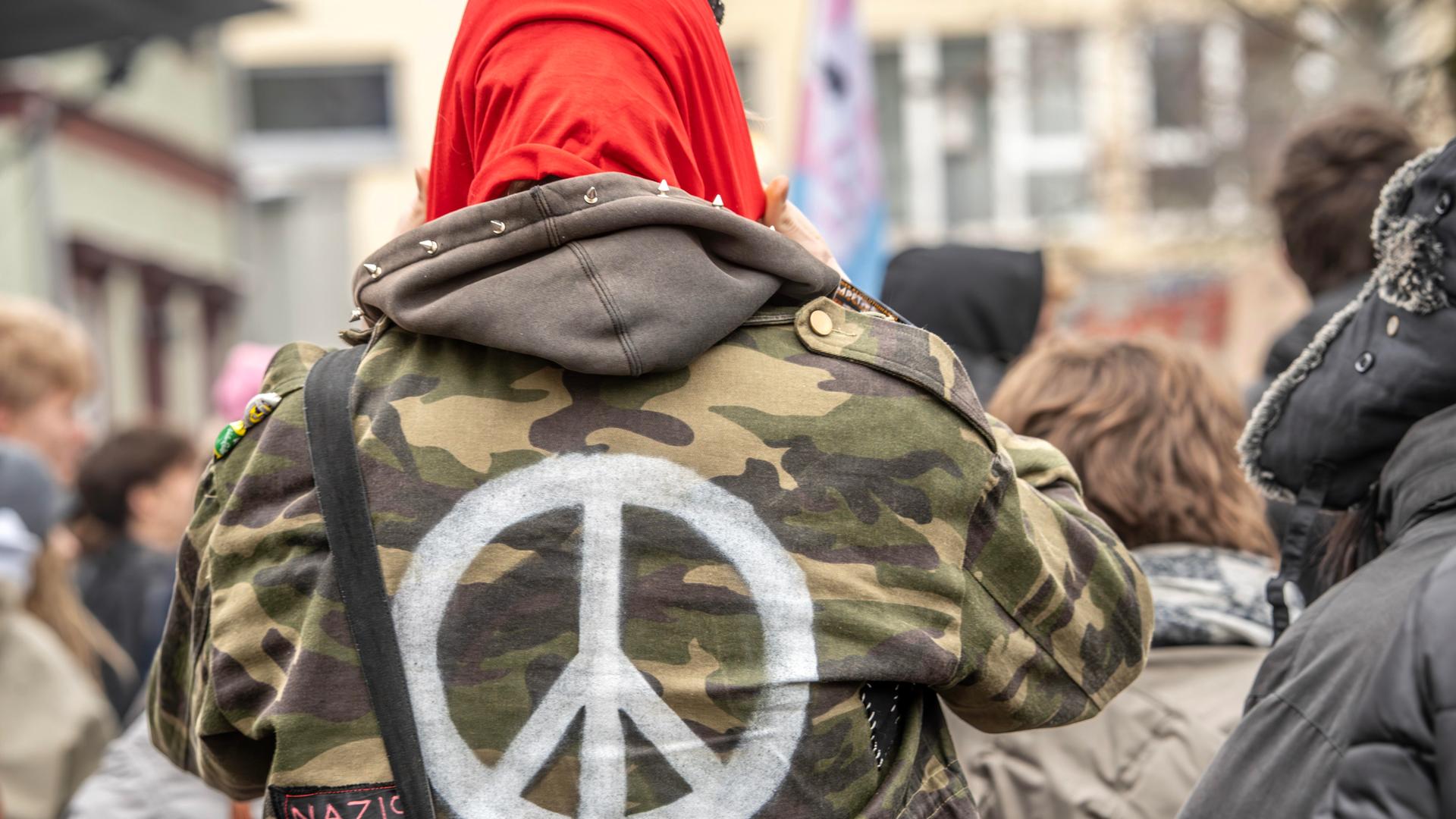 Ein Demonstrant trägt eine Bundeswehrjacke, auf die ein weißes Peace-Zeichen auf dem Rücken aufgemalt ist. Ein Demonstrant trägt eine Bundeswehrjacke, auf die ein weißes Peace-Zeichen auf dem Rücken aufgemalt ist.