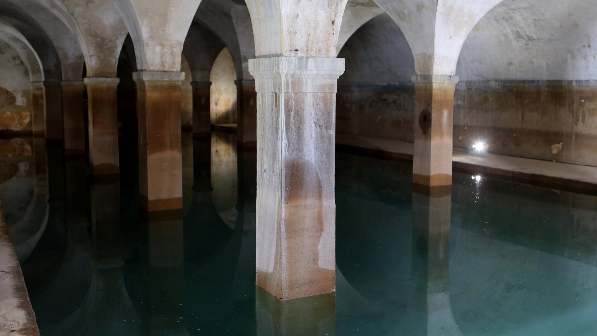 Säulen stehen in einem dunklen Raum, am Boden fließt Wasser.