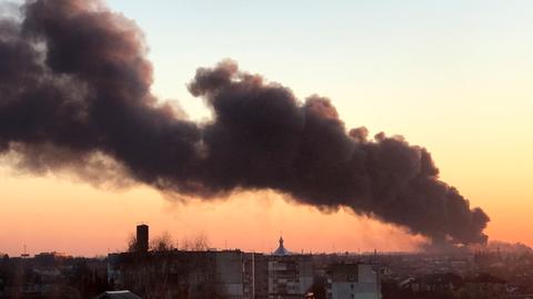 In der Dämmerung steicht eine dunkle Rauchsäule in einer Stadt auf. Es ist die ukrainische Stadt Lwiw.