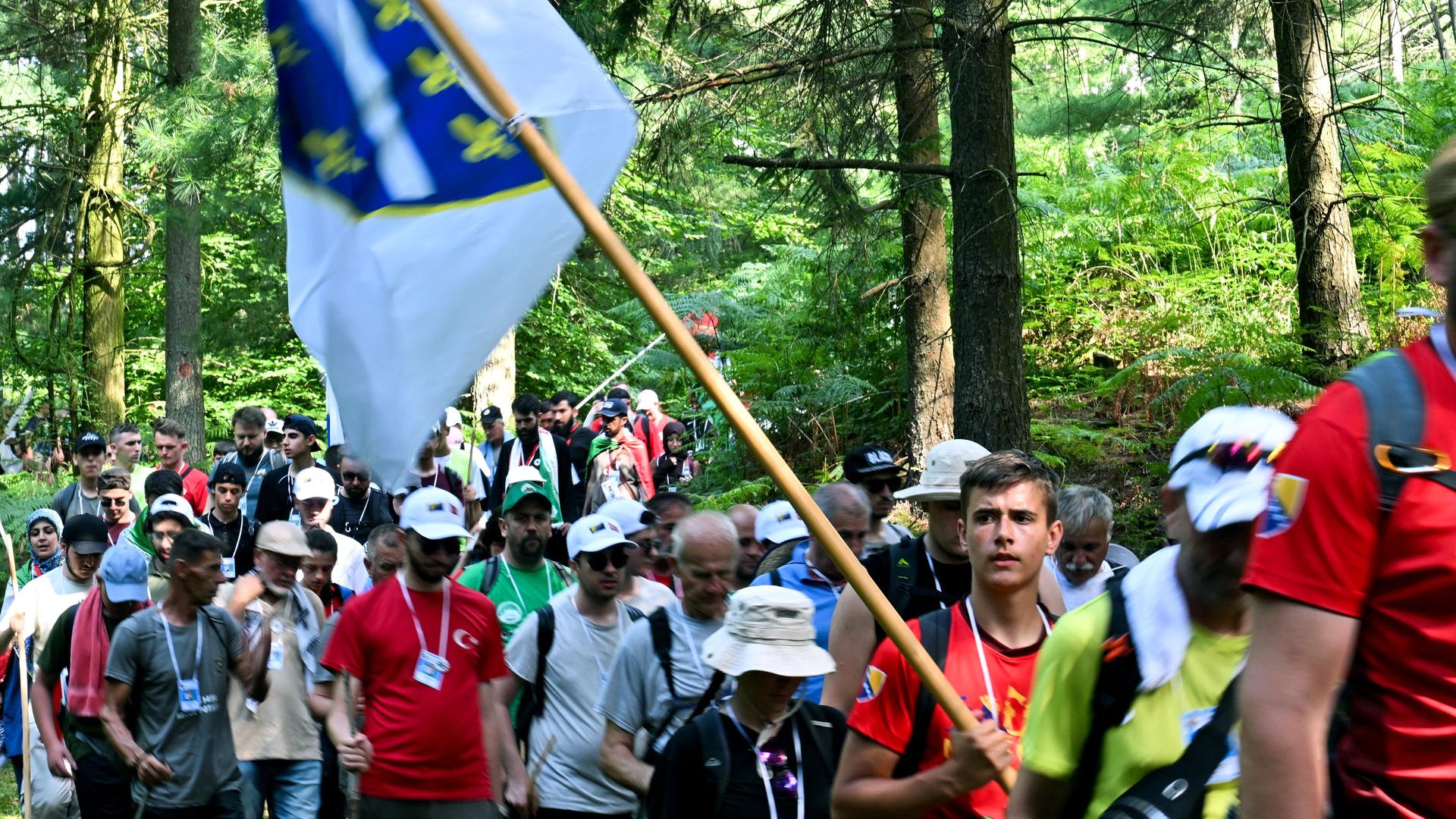Eine Menschengruppe läuft durch ein Waldstück. Ein junger Mann hält eine Flagge in der Hand.