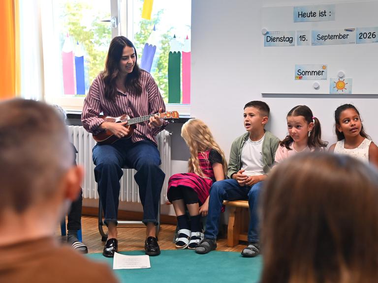 Eine Lehrerin spielt Ukulele. Die Schülerinnen und Schüler singen. Eine Lehrerin spielt Ukulele. Die Schülerinnen und Schüler singen.