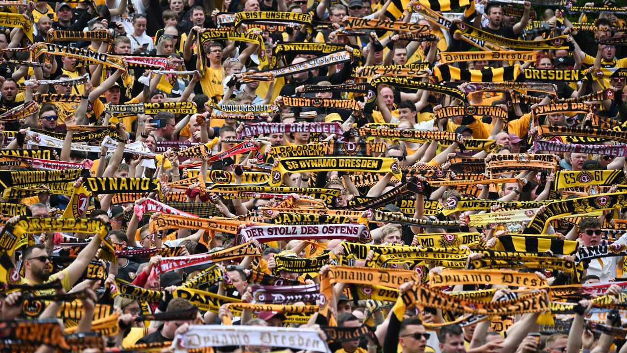 Fans von Dynamo Dresden stehen dichtgedrängt und halten Schals in die Höhe