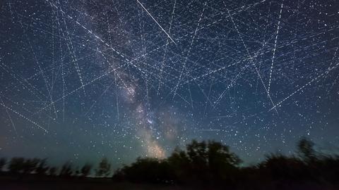 Ein mit Satelliten gefüllten Himmel in einer Sommernacht, in einer Langzeitbelichtung über einen Zeitraum von 30 Minuten aufgenommen. Viele der parallelen Streifen, die horizontal verlaufen, können von SpaceX Starlinks stammen.