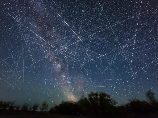 Ein mit Satelliten gefüllten Himmel in einer Sommernacht, in einer Langzeitbelichtung über einen Zeitraum von 30 Minuten aufgenommen. Viele der parallelen Streifen, die horizontal verlaufen, können von SpaceX Starlinks stammen.
