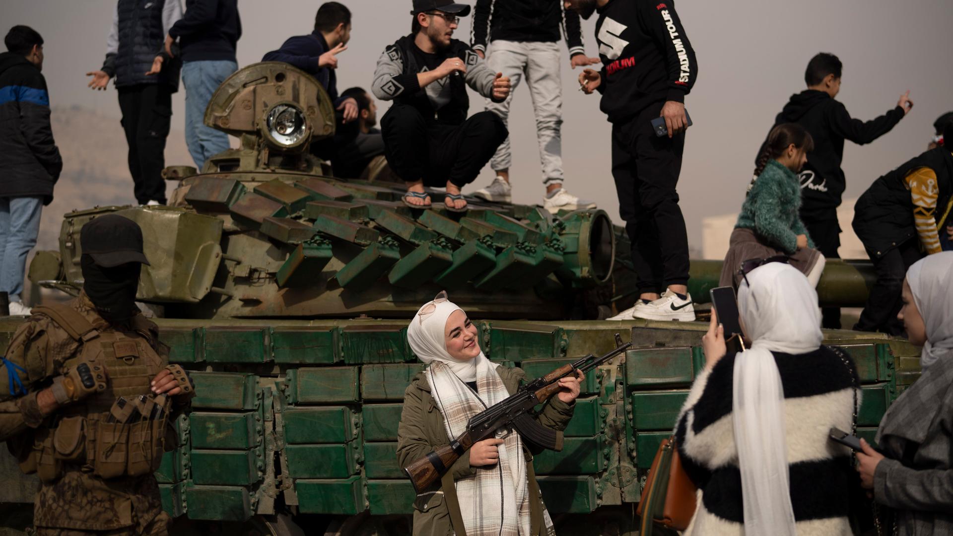 Eine Frau, die ein von einem syrischen Oppositionskämpfer geliehenes Gewehr in der Hand hält, posiert auf dem Umayyad-Platz in Damaskus für ein Foto neben einem Panzer der Regierungstruppen, der auf der Straße zurückgelassen wurde. 