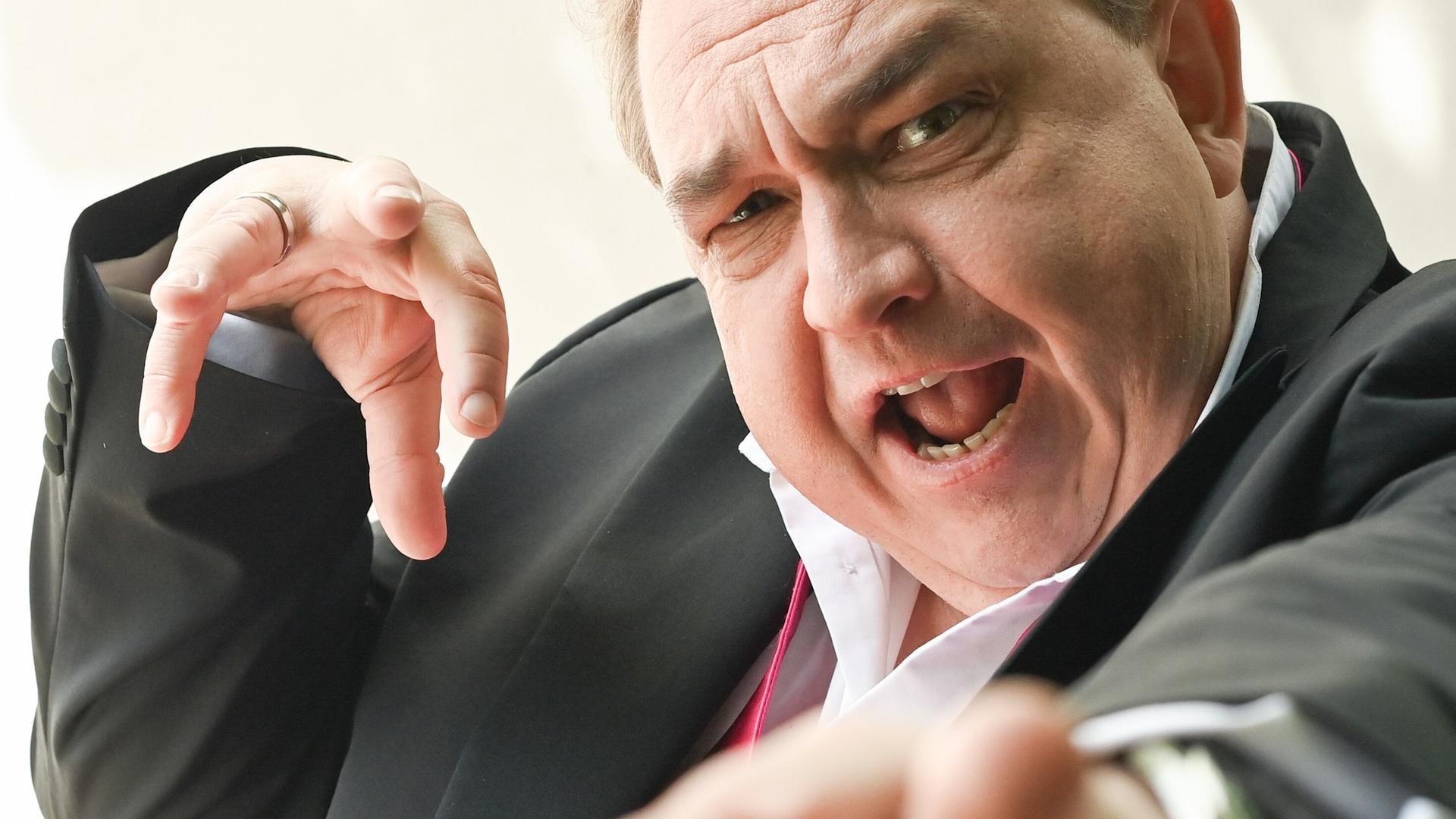 Oliver Kalkofe hat die Hände erhoben, als würde er einen Zauberspruch in Richtung der Kamera schicken.