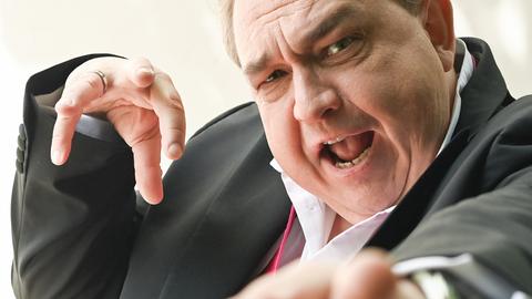 Oliver Kalkofe hat die Hände erhoben, als würde er einen Zauberspruch in Richtung der Kamera schicken.