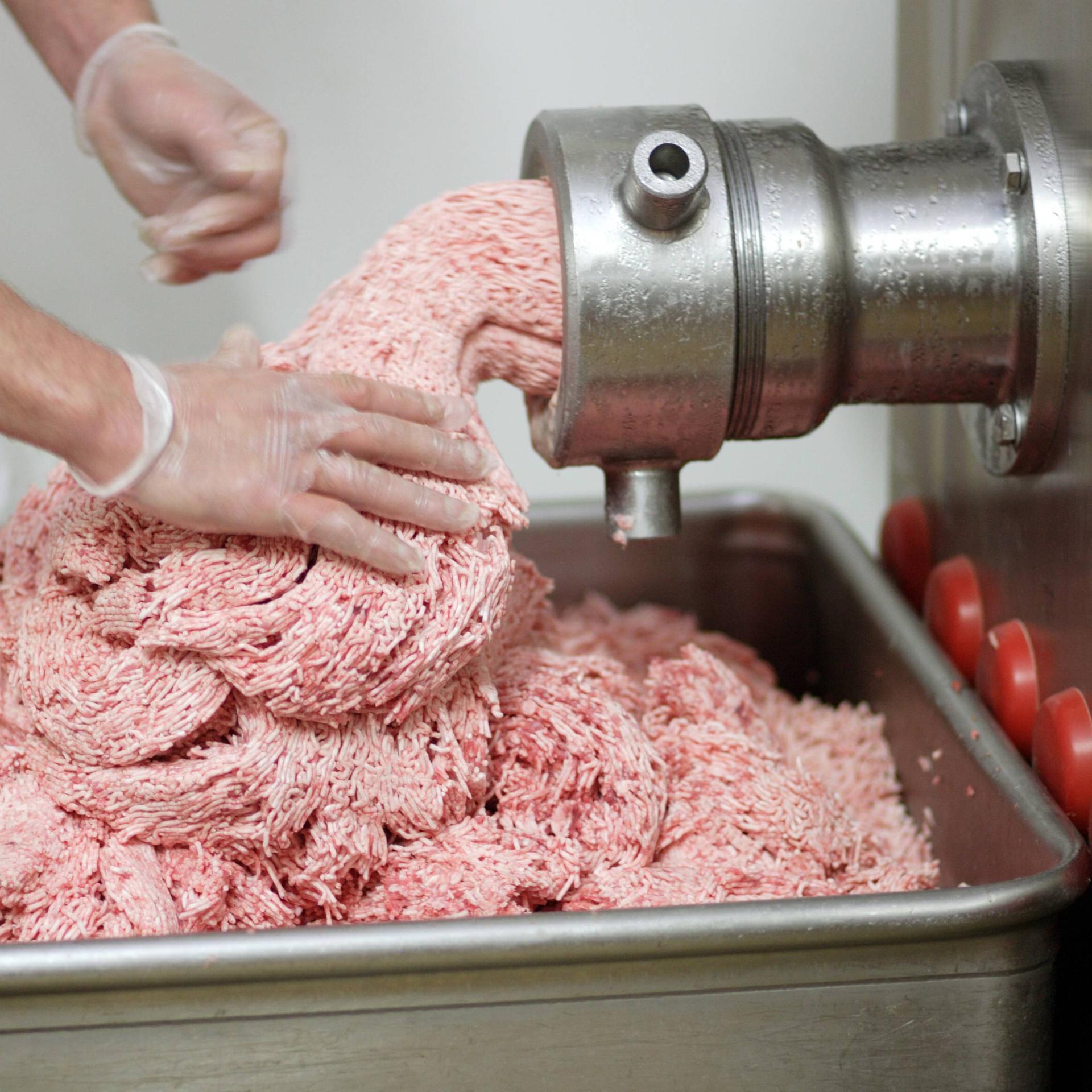 Ein Mann steht vor einem Fleischwolf aus dem Hackfleisch herauskommt und in einem roten Behälter davor landet.