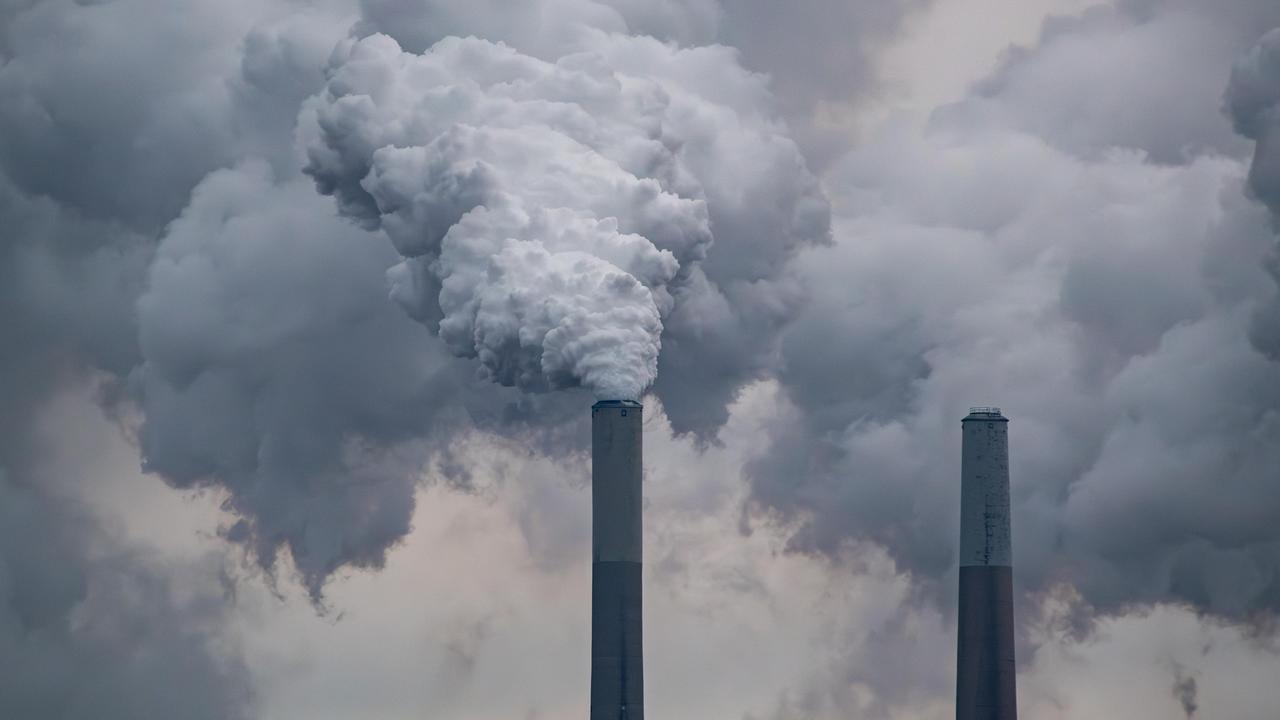 Zwei große Industrieschornsteine, aus denen dichte, grauweiße Rauchwolken in den Himmel aufsteigen und den Hintergrund fast vollständig verdecken.