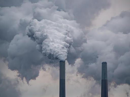 Zwei große Industrieschornsteine, aus denen dichte, grauweiße Rauchwolken in den Himmel aufsteigen und den Hintergrund fast vollständig verdecken.
