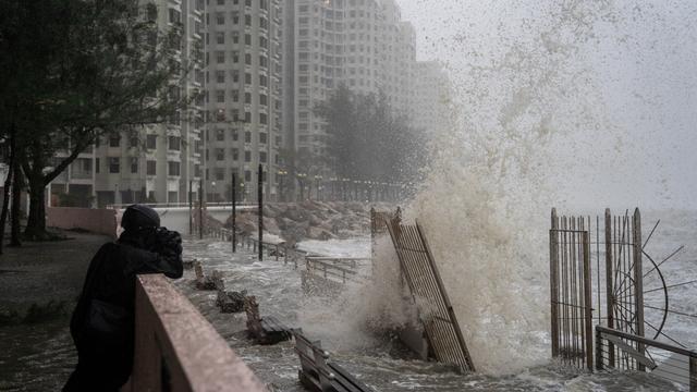 Ein Mann fotografiert hohe Wellen in Hongkong. Im Hintergrund sind Hoch-Häuser.