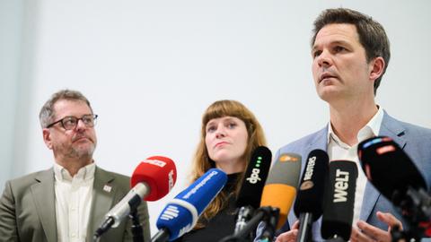Steffen Krach (r-l, SPD), Kerstin Wolter (Die Linke) und Werner Graf (Bündnis90/Die Grünen) stehen hinter Mikrofonen. 