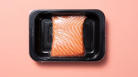 Ein Lachsfilet liegt vakuumverpackt auf einer rosa Oberfläche.