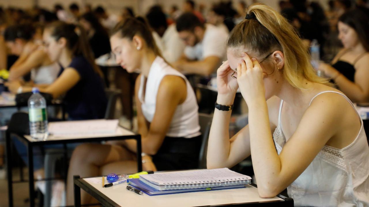 Ein Hörsaal mit Studierenden bei einer Prüfung, eine junge Frau vorne stützt ihren Kopf in den Händen ab