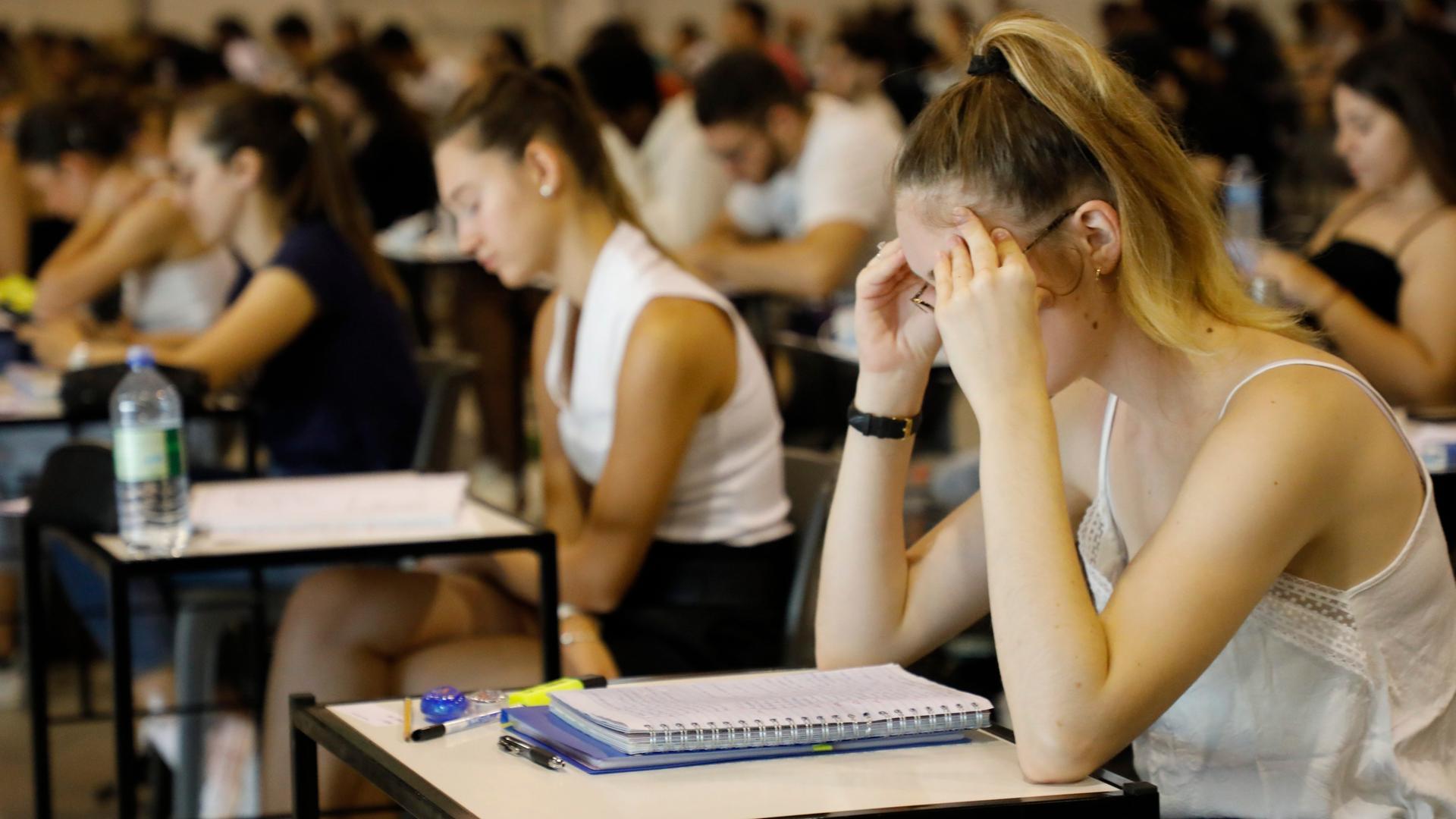 Ein Hörsaal mit Studierenden bei einer Prüfung, eine junge Frau vorne stützt ihren Kopf in den Händen ab
