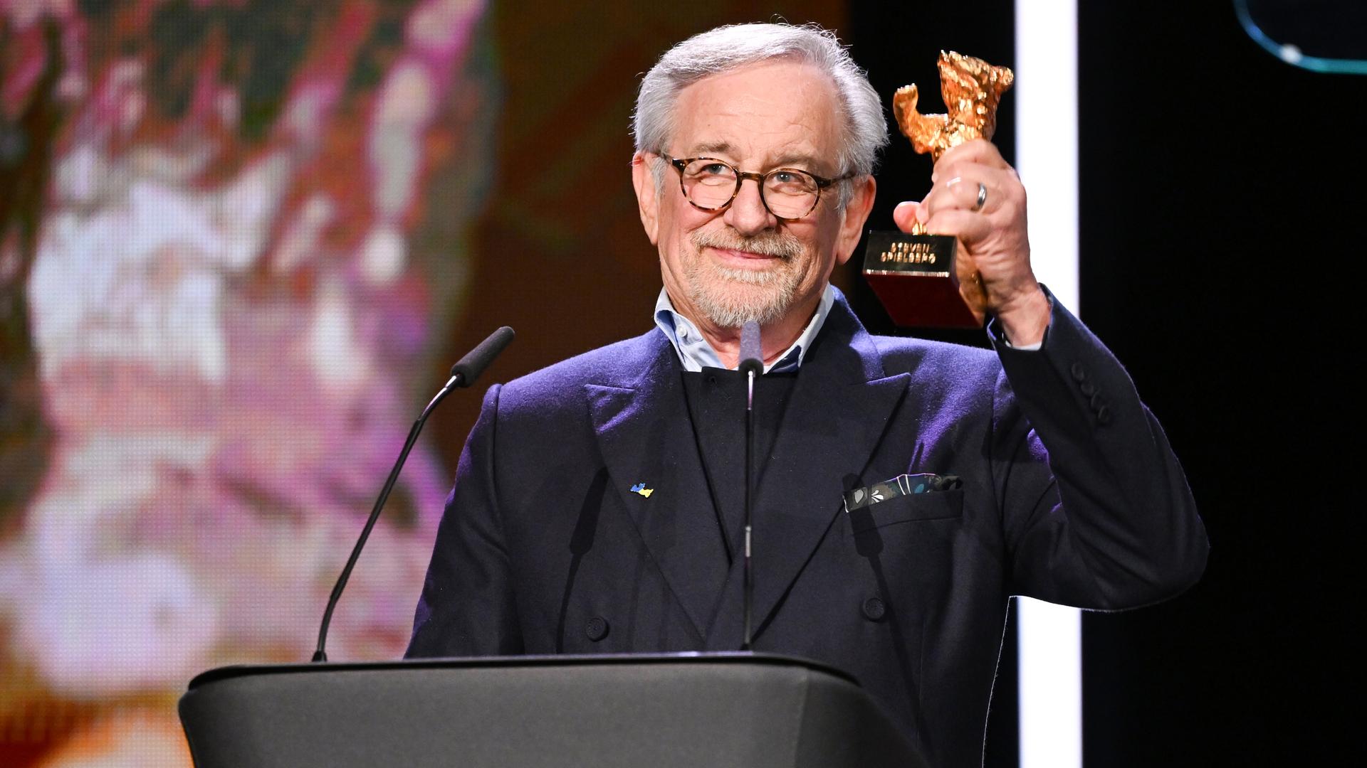 Steven Spielberg steht an einem Redner-Pult und hält den Goldenen Ehren-Bären hoch.