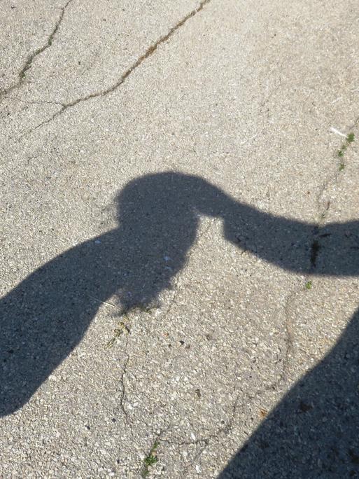 Der Schatten eines Kindes wird berührt von dem Schatten eines Erwachsenen.